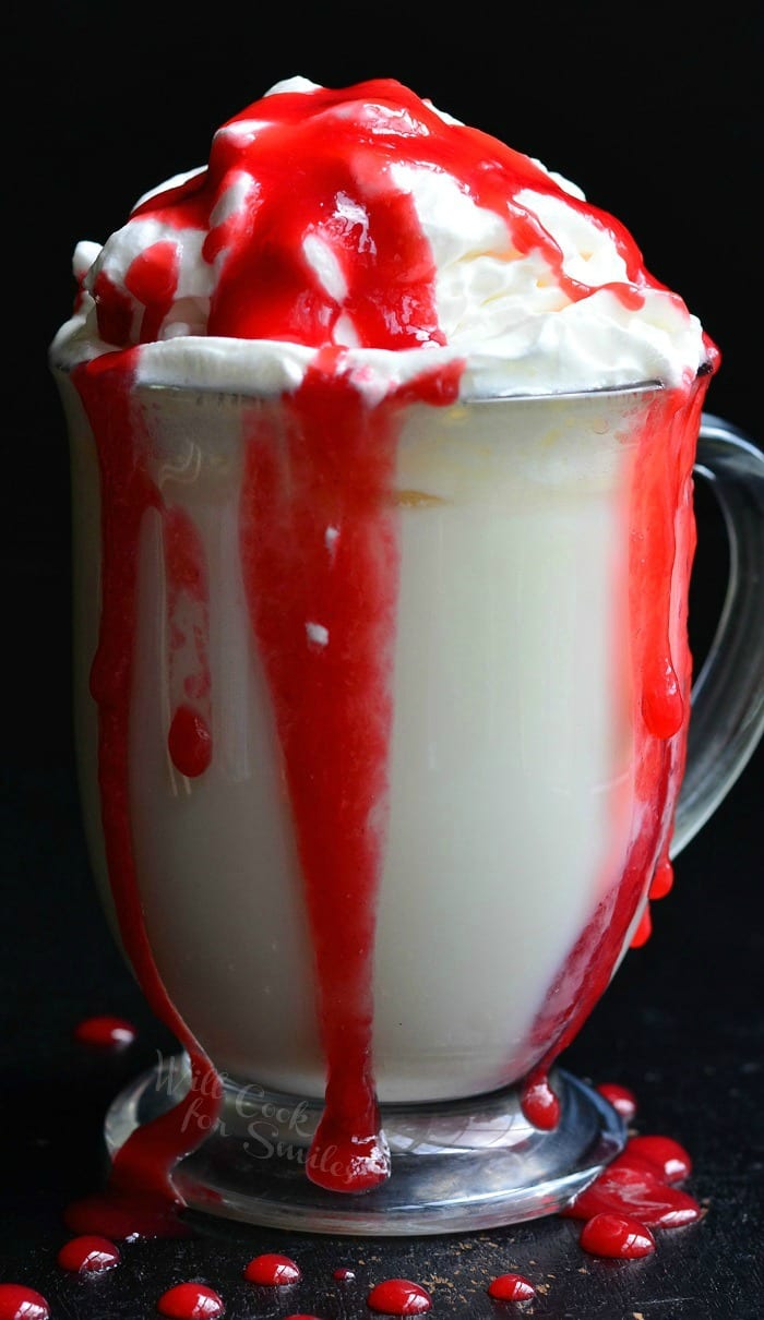 White Chocolate Raspberry Hot Chocolate in a clear glass bowl with whip cream and raspberry sauce on top 