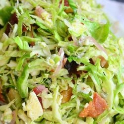 small white bowl filled with a bacon and blue brussels sprouts salad with warm bacon vinaigrette on a white table cloth covered table
