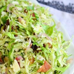 small white bowl filled with a bacon and blue brussels sprouts salad with warm bacon vinaigrette on a white table cloth covered table