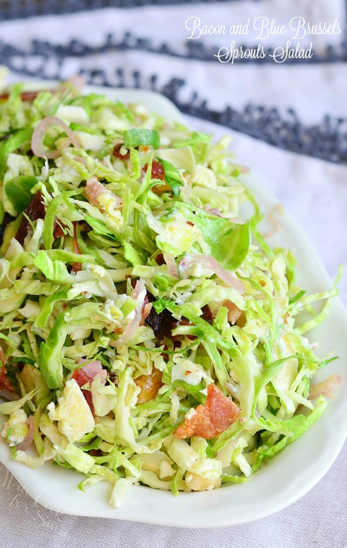 small white bowl filled with a bacon and blue brussels sprouts salad with warm bacon vinaigrette on a white table cloth covered table