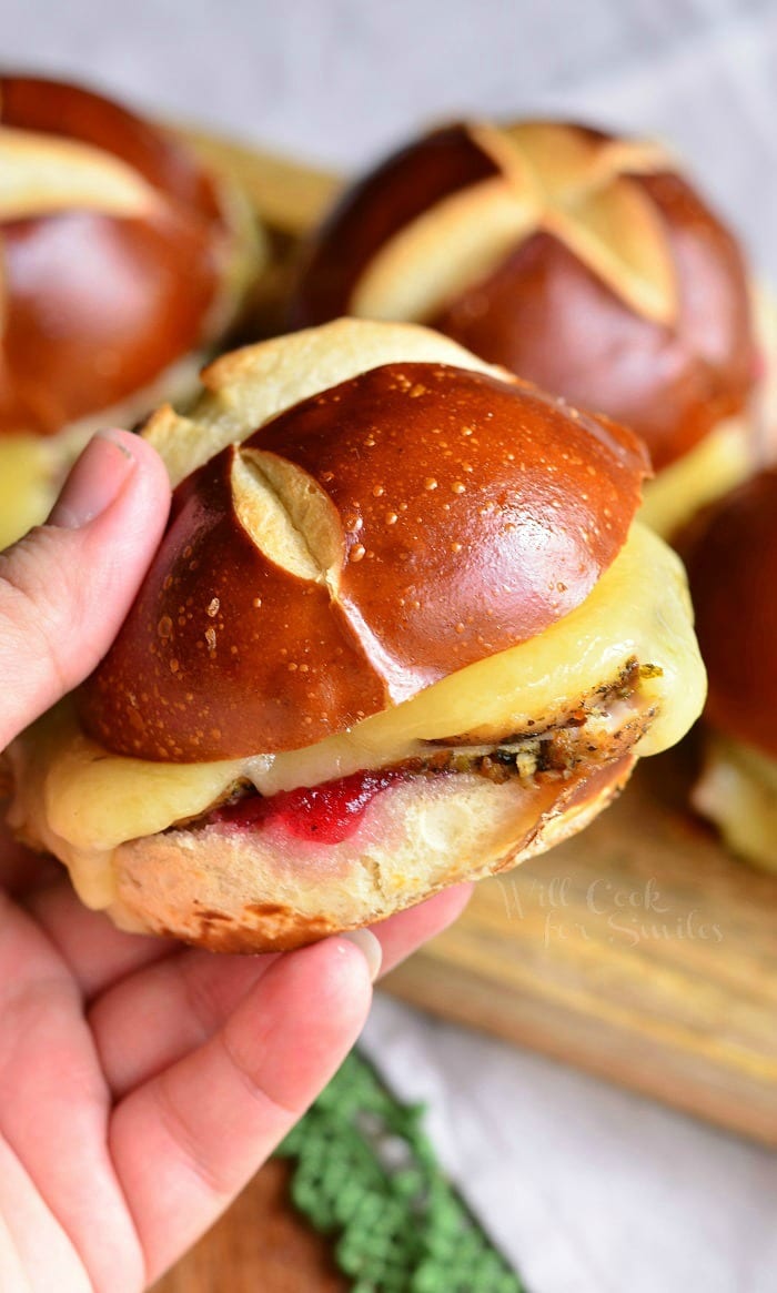 holding a Cranberry Asiago Turkey Sliders on a pretzel bun with cheese, turkey, and cranberry sauce 