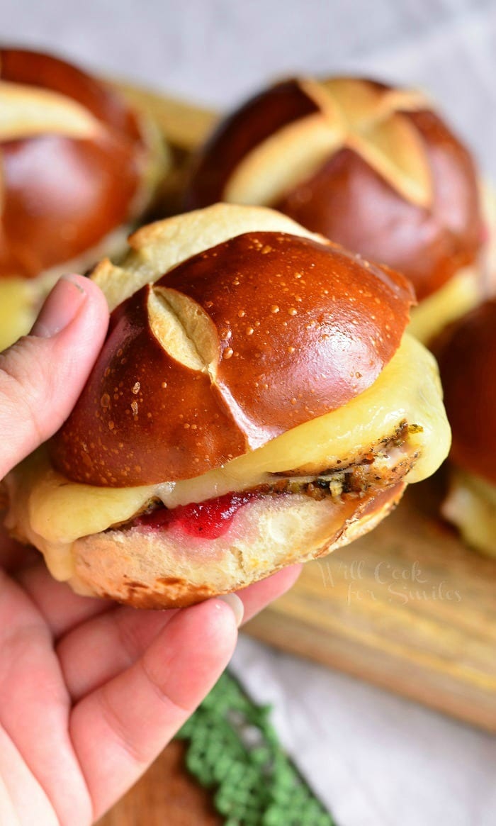 Holding a Cranberry Asiago Turkey Sliders that's on a pretzel bun 