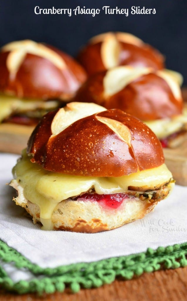 3 cranberry asiago turkey sliders on a wooden cutting board and 1 slider on a white cloth in the foreground