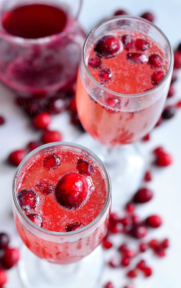 top view close up of Cranberry Pomegranate Champagne Cocktail in a champagne glass with Pomegranate and cranberries in the glass as garnish and around the bottom of the glass 