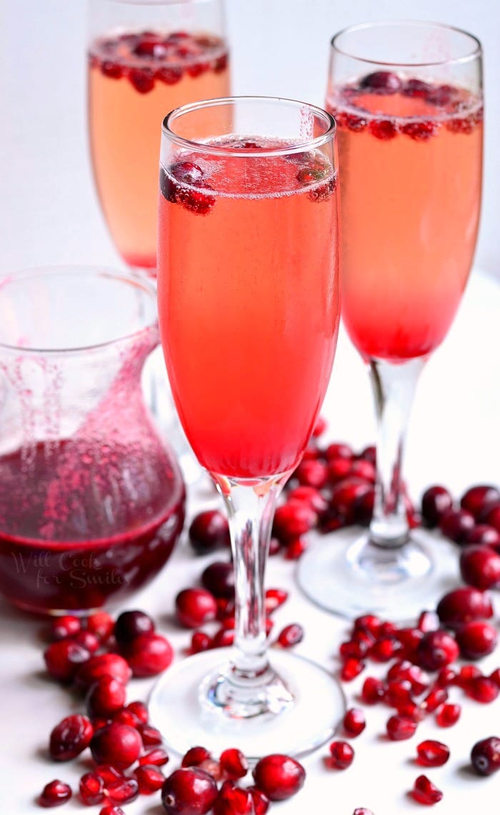 Cranberry Pomegranate Champagne Cocktail in a champagne glass with Pomegranate and cranberries in the glass as garnish and around the bottom of the glass 