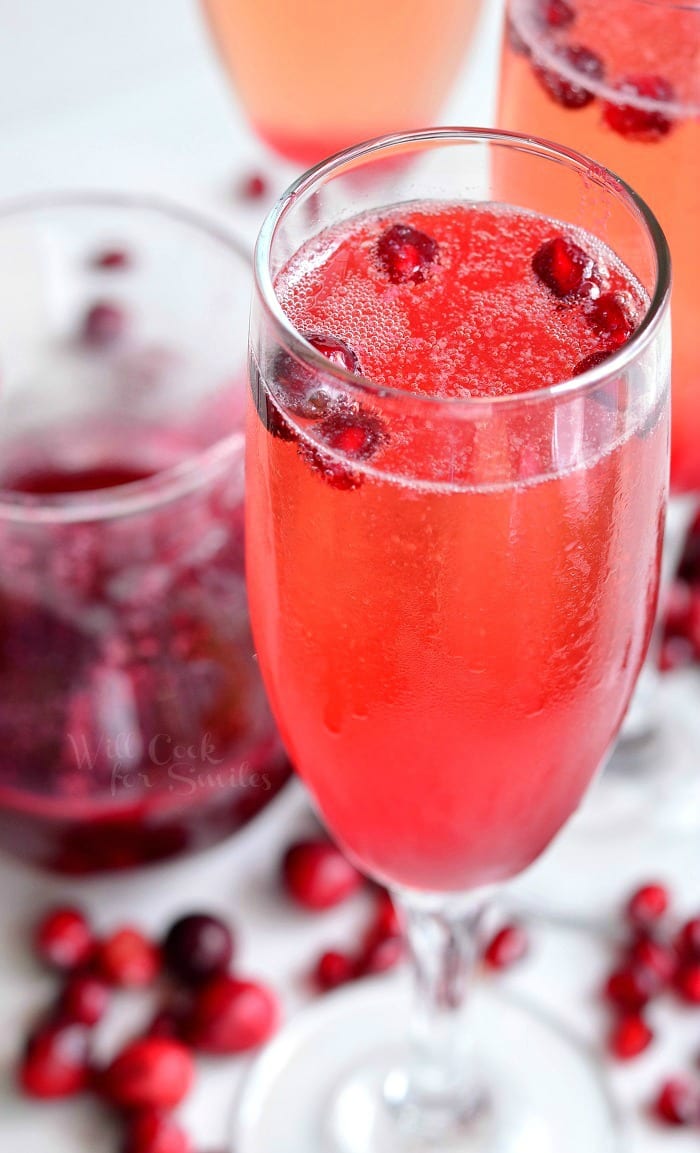 Cranberry Pomegranate Champagne Cocktail in a champagne glass with Pomegranate and cranberries in the glass as garnish and around the bottom of the glass 