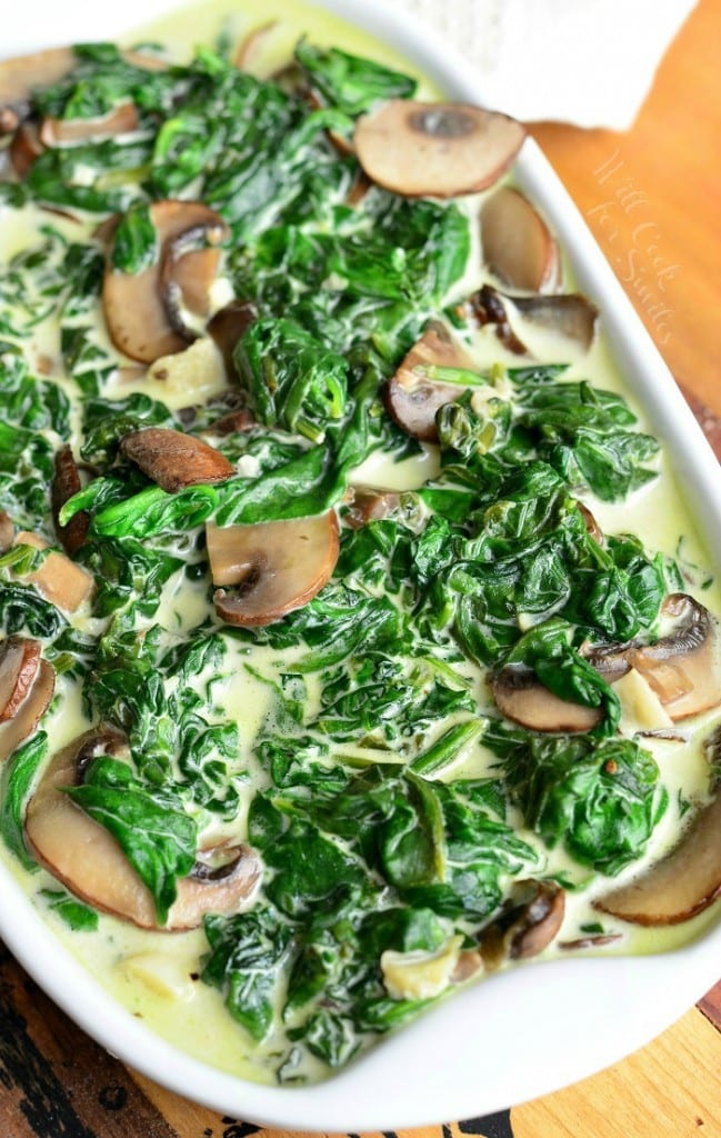 white baking pan filled with creamed spinach and mushroom in white wine sauce on a wooden table with a white cloth behind as viewed from above