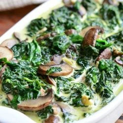 white baking pan filled with creamed spinach and mushroom in white wine sauce on a wooden table with a white cloth behind