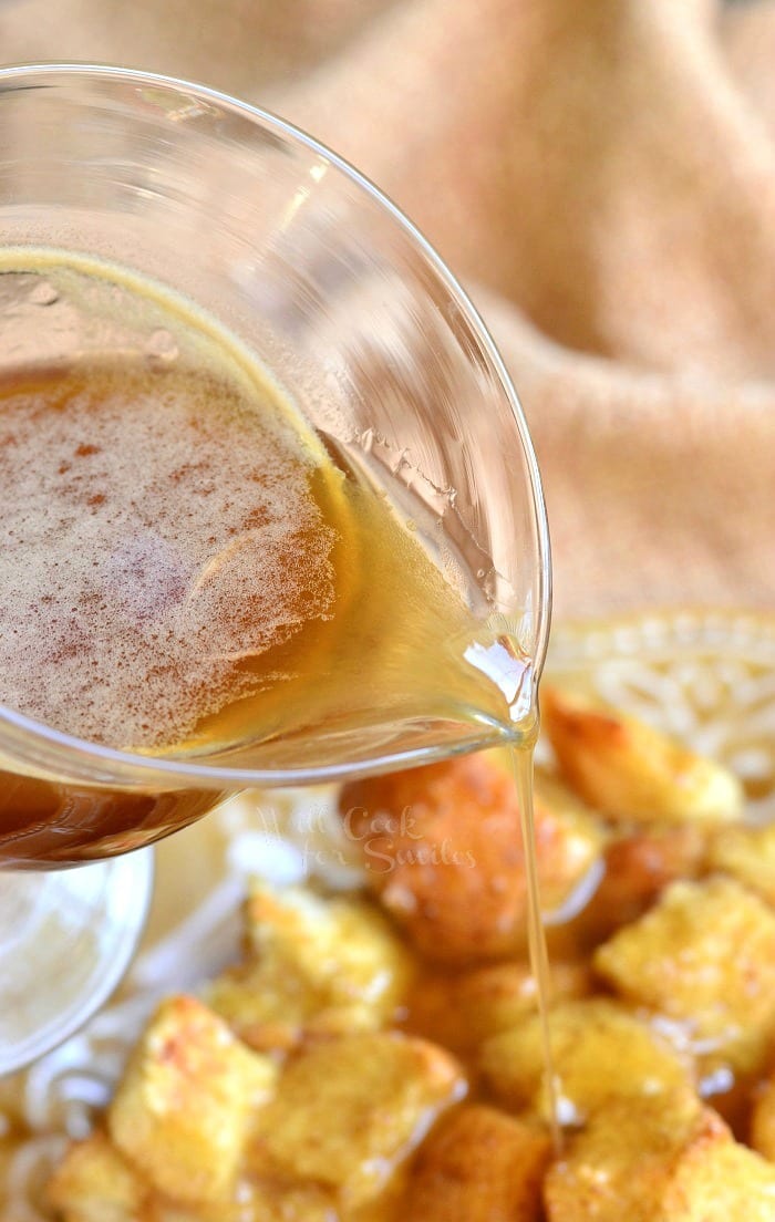 pouring butter brandy sauce over Eggnog Bread Pudding that is on plate 