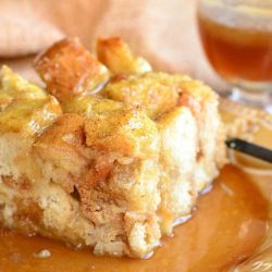 one portion of holiday nog bread pudding with butter brandy sauce on a decorative plate with a brown cloth in the background viewed close up