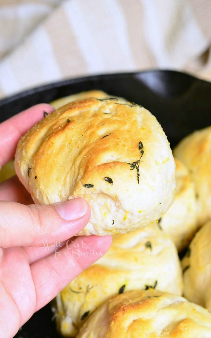 Holding a Biscuit with thyme on it with the rest in a cast iron skillet 