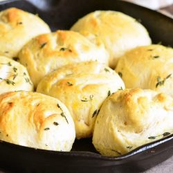 black skillet holding lemon thyme biscuits on a wooden table with a white and tan cloth in the background viewed close up