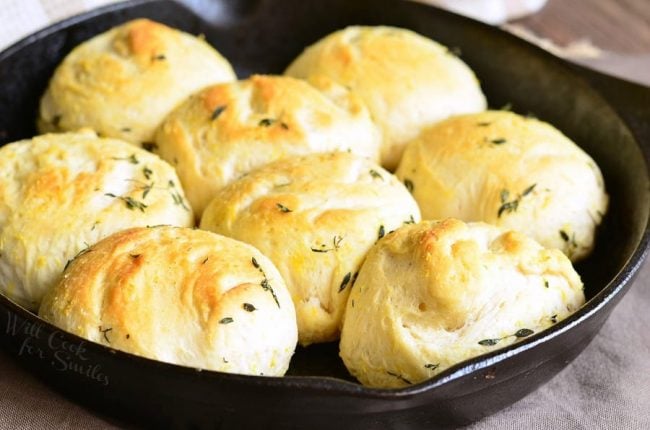 A skillet filled with freshly baked golden brown garlic and herb dinner rolls. The rolls are fluffy and lightly sprinkled with herbs, creating a rustic and appetizing look.