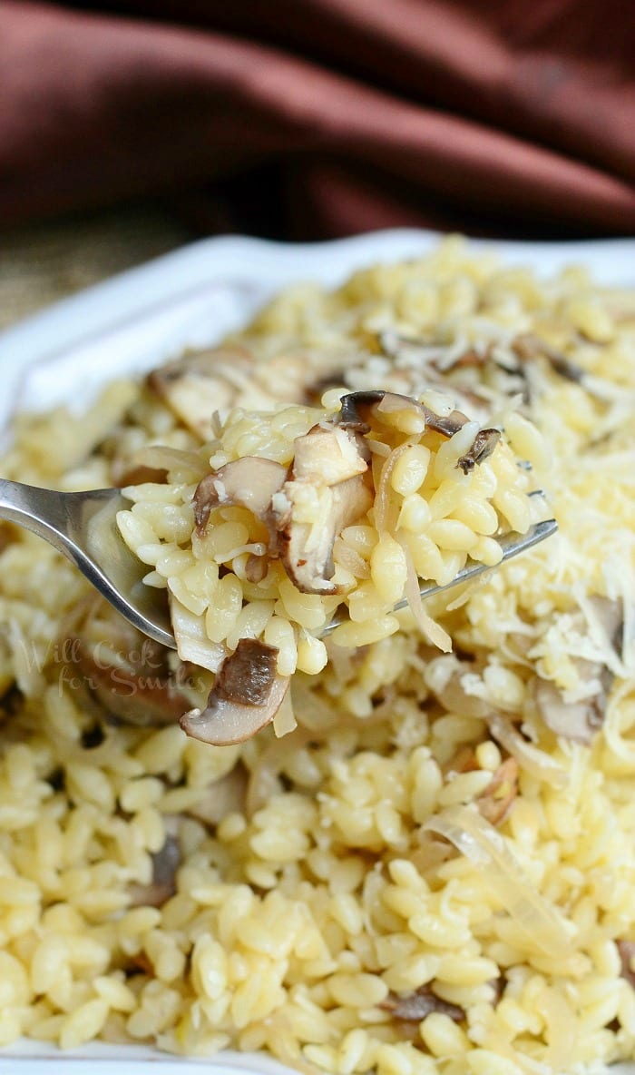 Orzo with Mushroom and parmesan cheese on a white serving dish with a fork scooping some out 