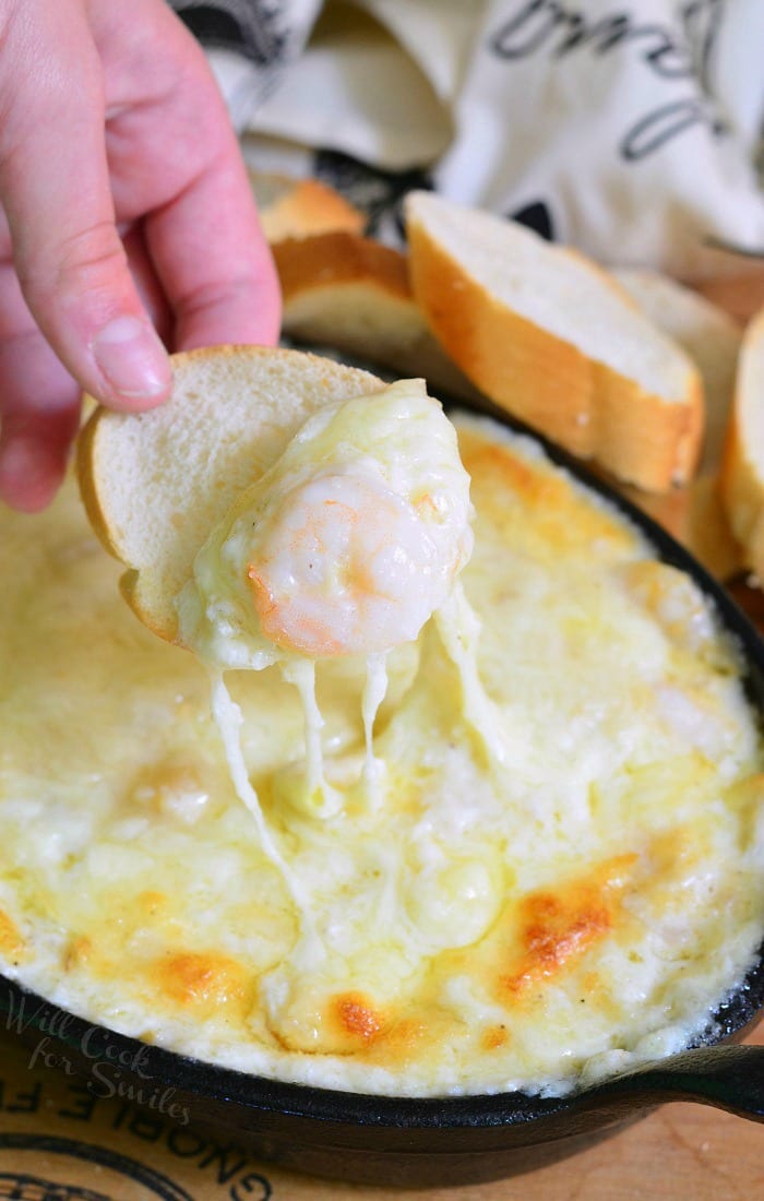 dipping a slice of french bread into Seafood & Cheese Dip with a shrimp on the bread that is a cast iron pan 