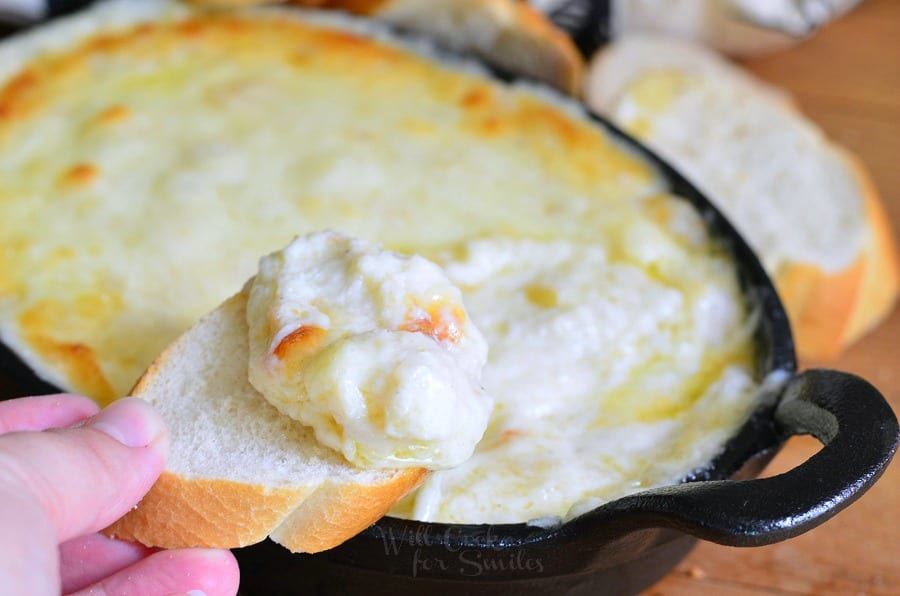 dipping a slice of french bread into Seafood & Cheese Dip that is a cast iron pan 