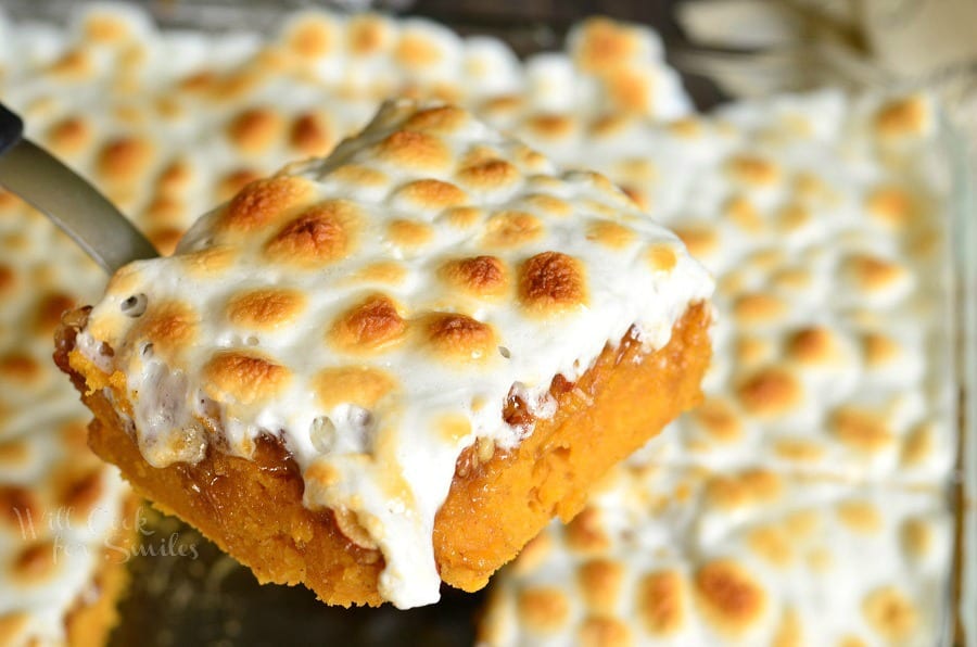 sweet potato casserole with marshmallow topping being lifted out of glass baking pan with a spatula 