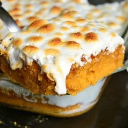 1 portion of sweet potato casserole cake being held above the rest of the cake in a glass baking pan on a black pan