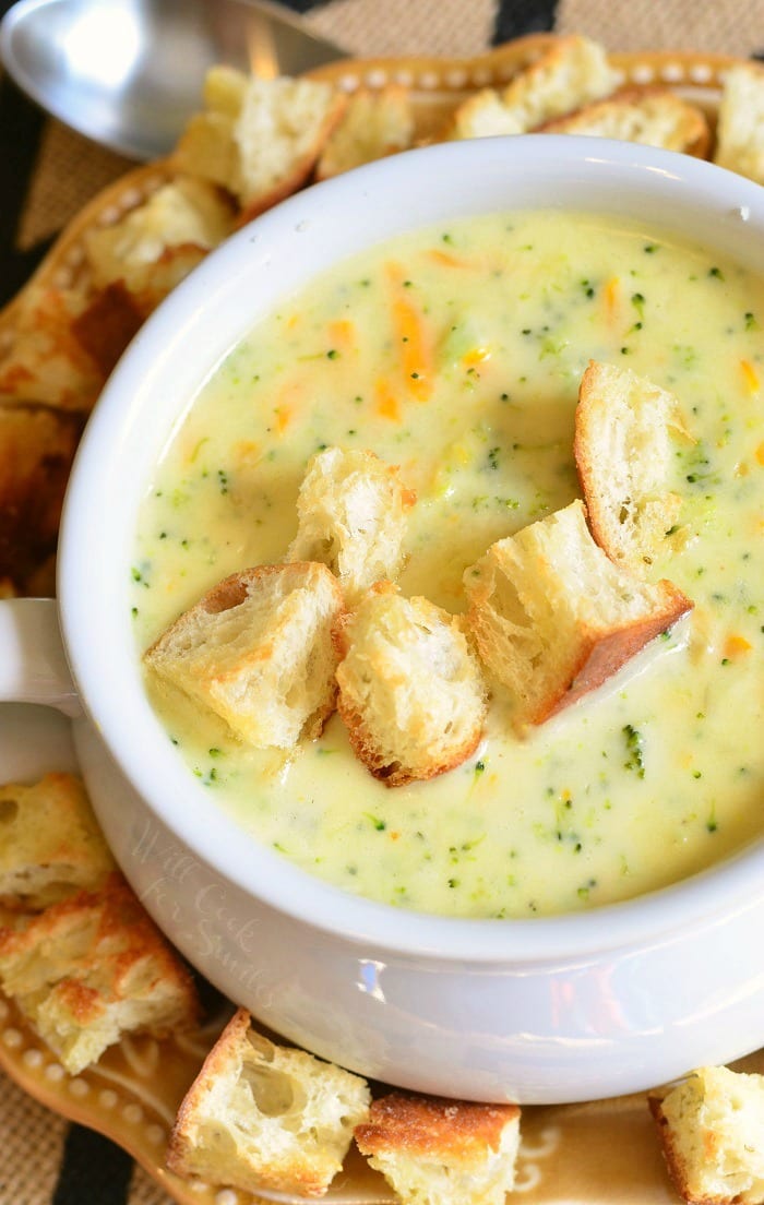 top view Asiago Broccoli Cheese Soup in a white soup bowl with cut up pieces of crusty bread on top and around the bottom of the bowl