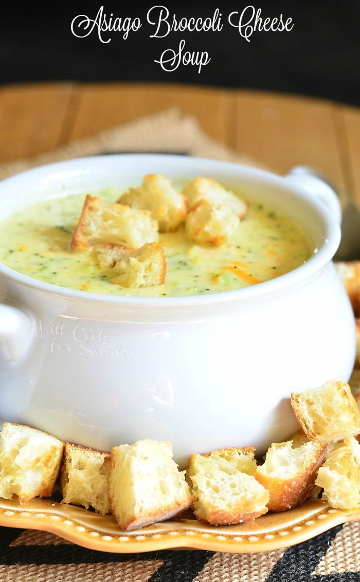 Asiago Broccoli Cheese Soup in a white soup bowl with cut up pieces of crusty bread on top and around the bottom of the bowl