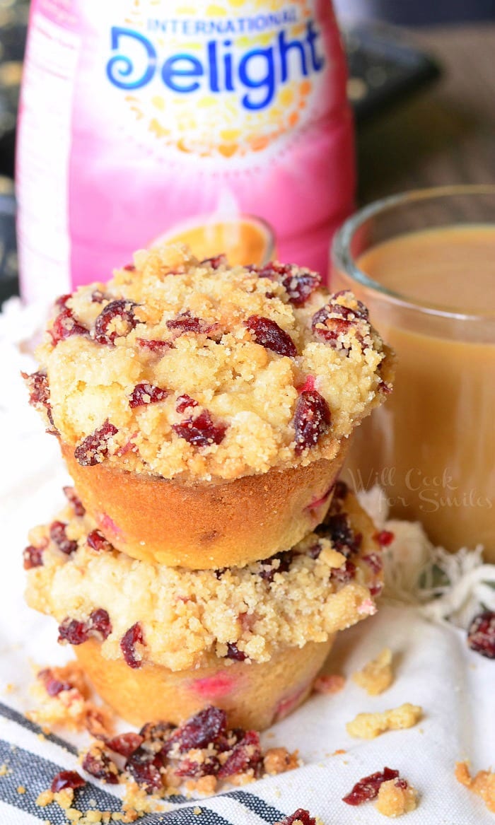 Cranberry White Chocolate Chip Streusel Muffins stacked up next to a clear glass of coffee and creamer in the background