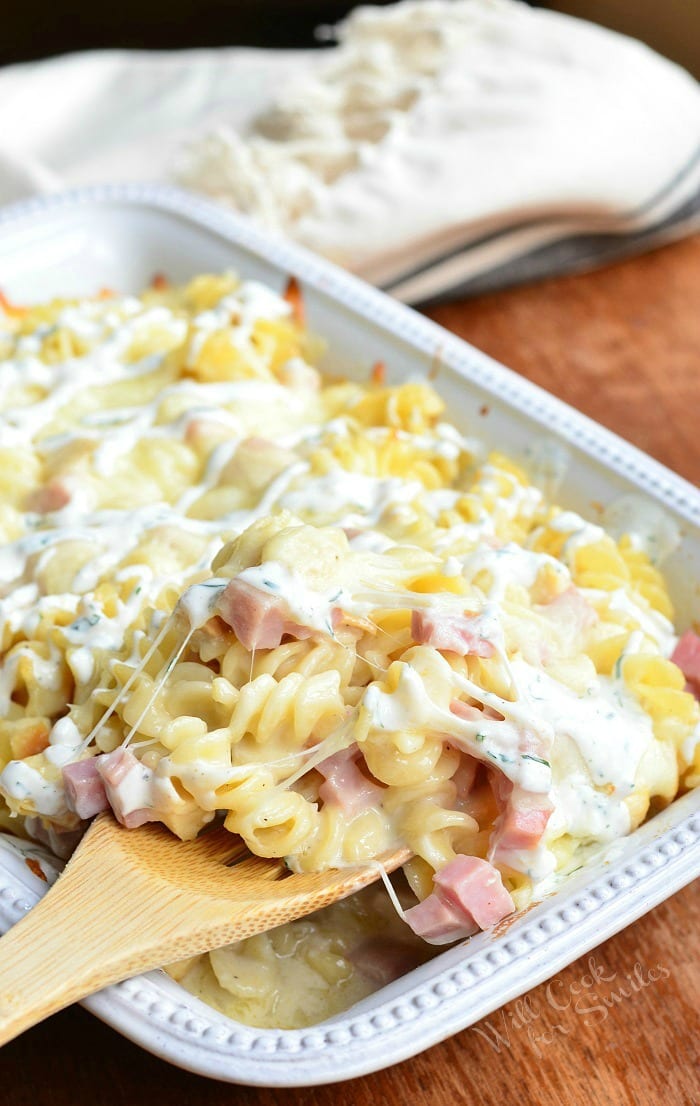 Chicken Cordon Bleu pasta with cork screw pasta and ham in a cheese sauce in a white casserole dish with a wooden spoon
