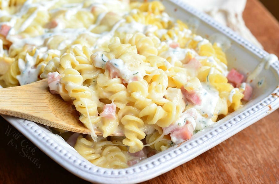 Chicken Cordon Bleu pasta with cork screw pasta and ham in a cheese sauce in a white casserole dish with a wooden spoon