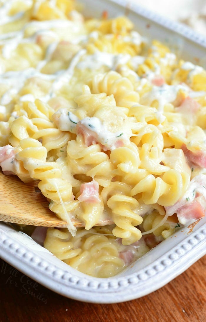 Chicken Cordon Bleu pasta with cork screw pasta and ham in a cheese sauce in a white casserole dish with a wooden spoon