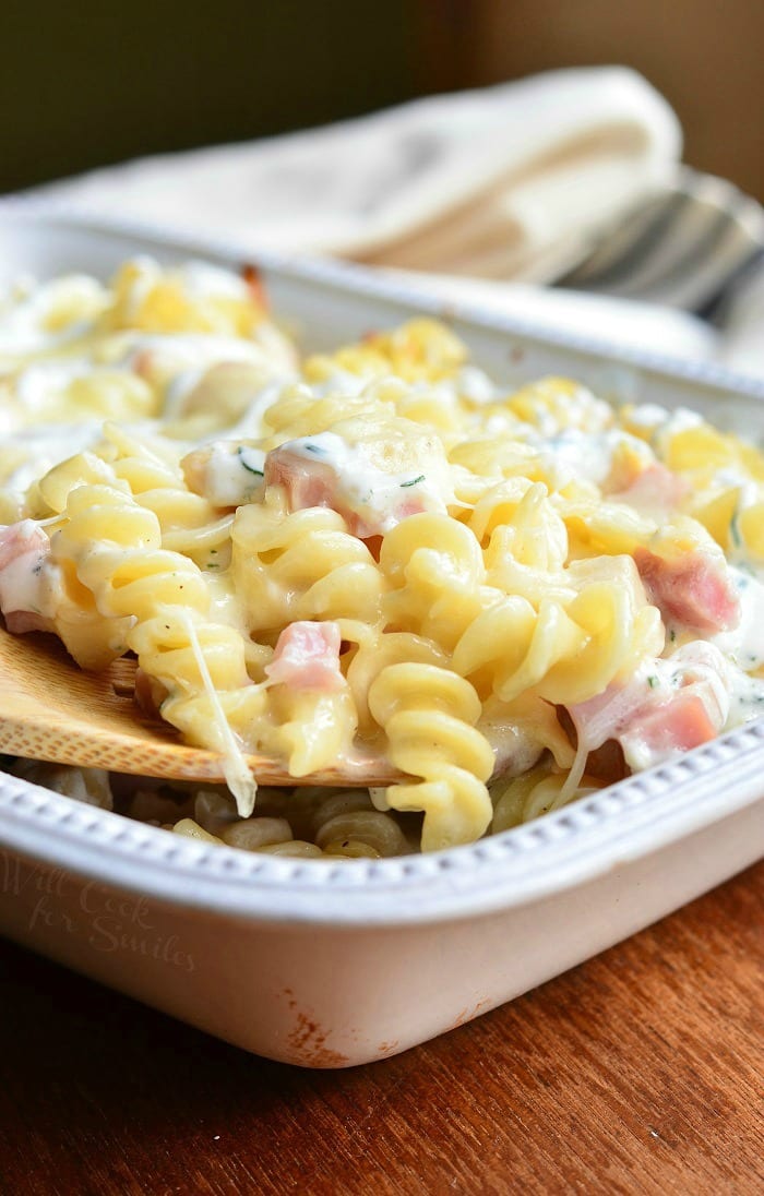 Chicken Cordon Bleu pasta with cork screw pasta and ham in a cheese sauce in a white casserole dish with a wooden spoon