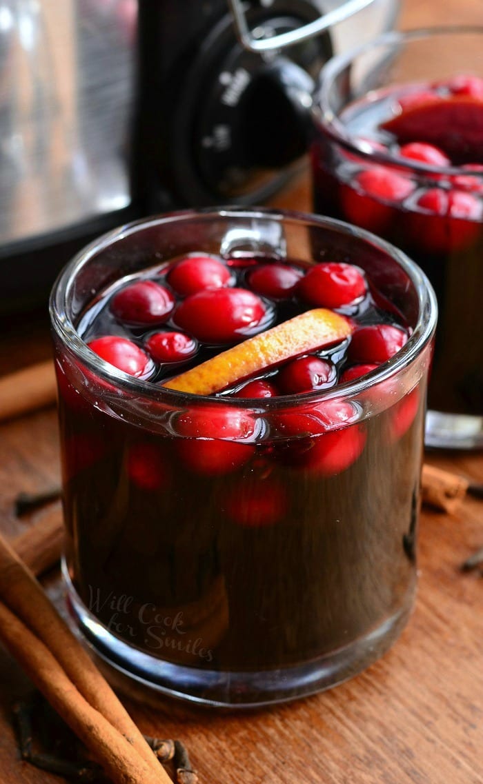 Orange Cranberry Sangria in a glass mug with orange and cranberries inside on a table with cinnamon sticks around it 