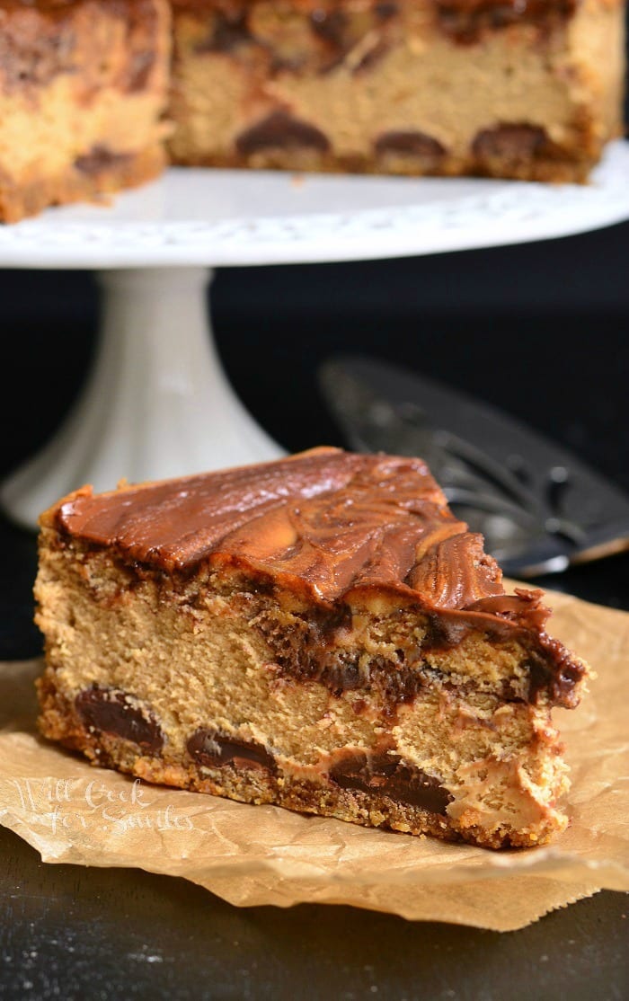 slice of Gingerbread Nutella Swirl Cheesecake on a piece of butcher paper with the rest of the cheesecake on a cake stand 