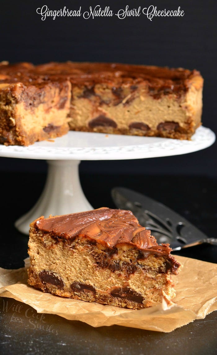 slice of Gingerbread Nutella Swirl Cheesecake on a piece of butcher paper with the rest of the cheesecake on a cake stand 