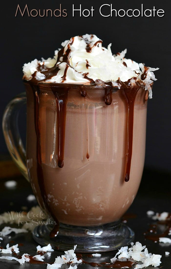 Hot Chocolate in a clear glass with whipped cream, chocolate sauce, and shredded coconut on top  