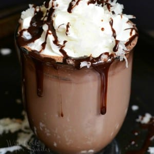 glass coffee mug filled with Mounds Hot Chocolate topped with whipped cream and coconut shavings while additional shavings are scattered around the base of the mug.