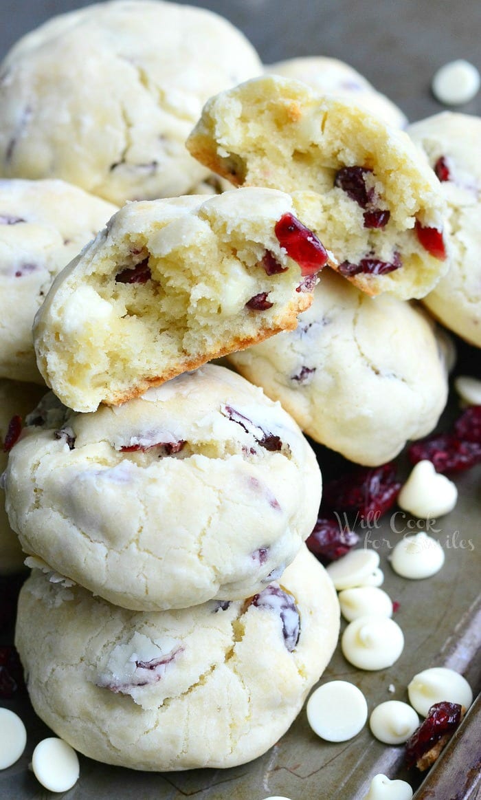 White Chocolate cookies with Cranberries with top one cut in half staked on a cutting board with white chocolate chips 