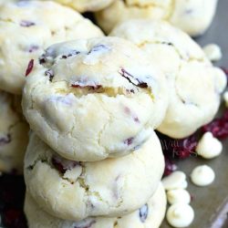 stacked white chocolate cranberry soft and chewy crinkle cookies on a baking sheet tray with white chocolate chips scattered around the cookies as viewed from the top