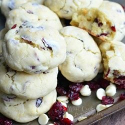 White chocolate cranberry soft and chewy crinkle cookies on a baking tray with cranberries and white chocolate chips scattered around cookies