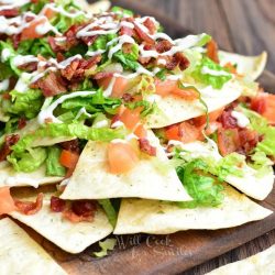 Wooden platter with BLT nachos and homemade baked cool ranch tortilla chips on a wooden table