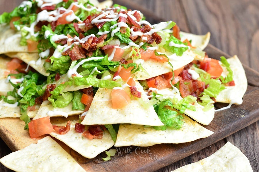 BLT Nachos with lettuce, tomato, and bacon on a wood cutting board 