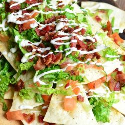 View from above of a wooden platter with BLT nachos and homemade baked cool ranch tortilla chips on a wooden table