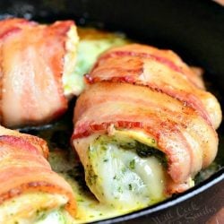 A black skillet with bacon wrapped mozzarella pesto stuffed chicken on a wooden table