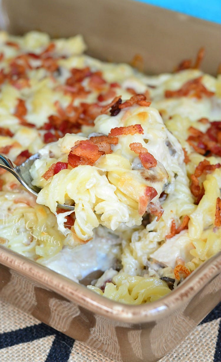 Chicken Bacon Alfredo Pasta Casserole in a casserole dish with a spoon scooping some out 