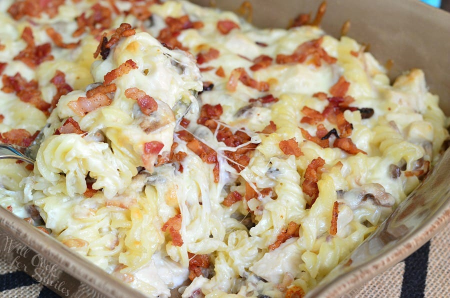 casserole pan filled with chicken bacon alfredo pasta casserole and scooping.