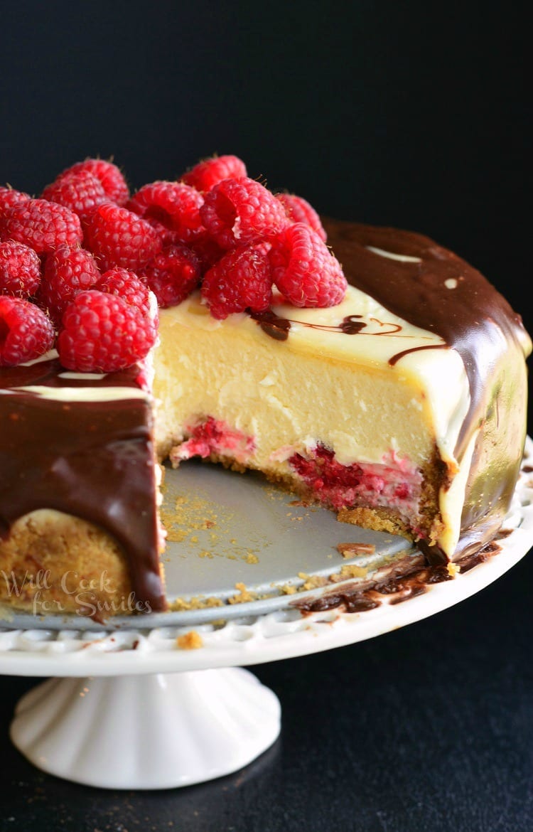 Double Chocolate Ganache and Raspberry Cheesecake with raspberries on top and a piece missing on a cake stand 