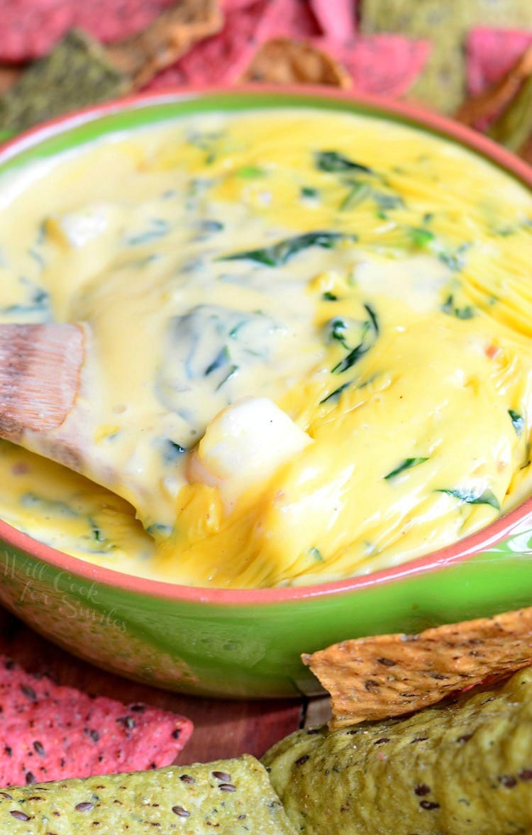 Shrimp and Spinach Queso Dip in a green bowl with a wooden spoon in it and tortilla chips around it 