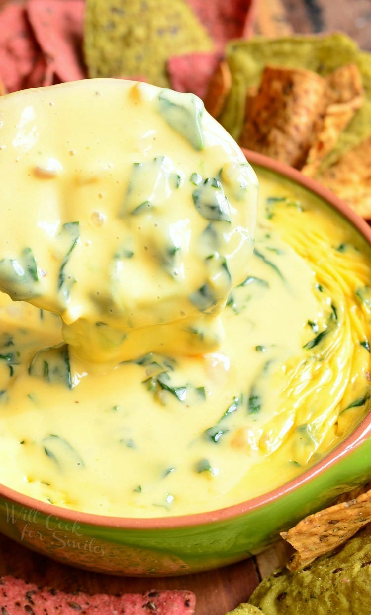 top view of Shrimp and Spinach Queso Dip in a green bowl with a wooden spoon scooping some out and tortilla chips around it 