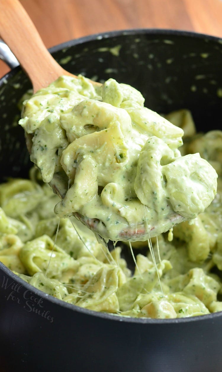 Pesto Alfredo Tortellini in a pot being scooped out with a wooden spoon 