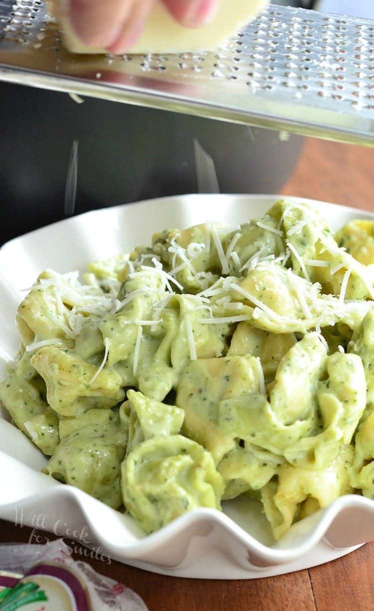 Pesto Alfredo Tortellini in a white serving bowl with parmesan cheese on top 