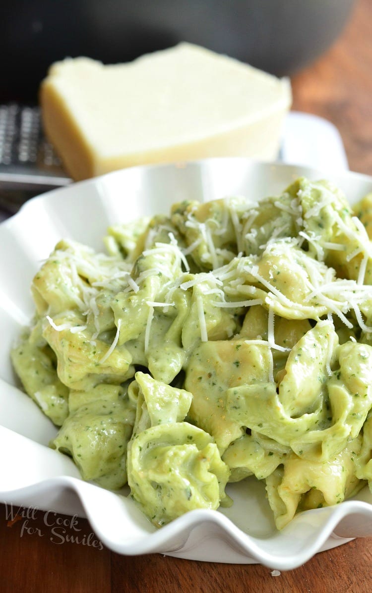 Pesto Alfredo Tortellini in a bowl with cheese on the side on a wood table 