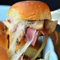 1 corned beef slider on a silver spatula held above a baking dish with additional sliders as seen from the front